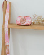 Floral-patterned pouch and strap on a wooden shelf with a white background