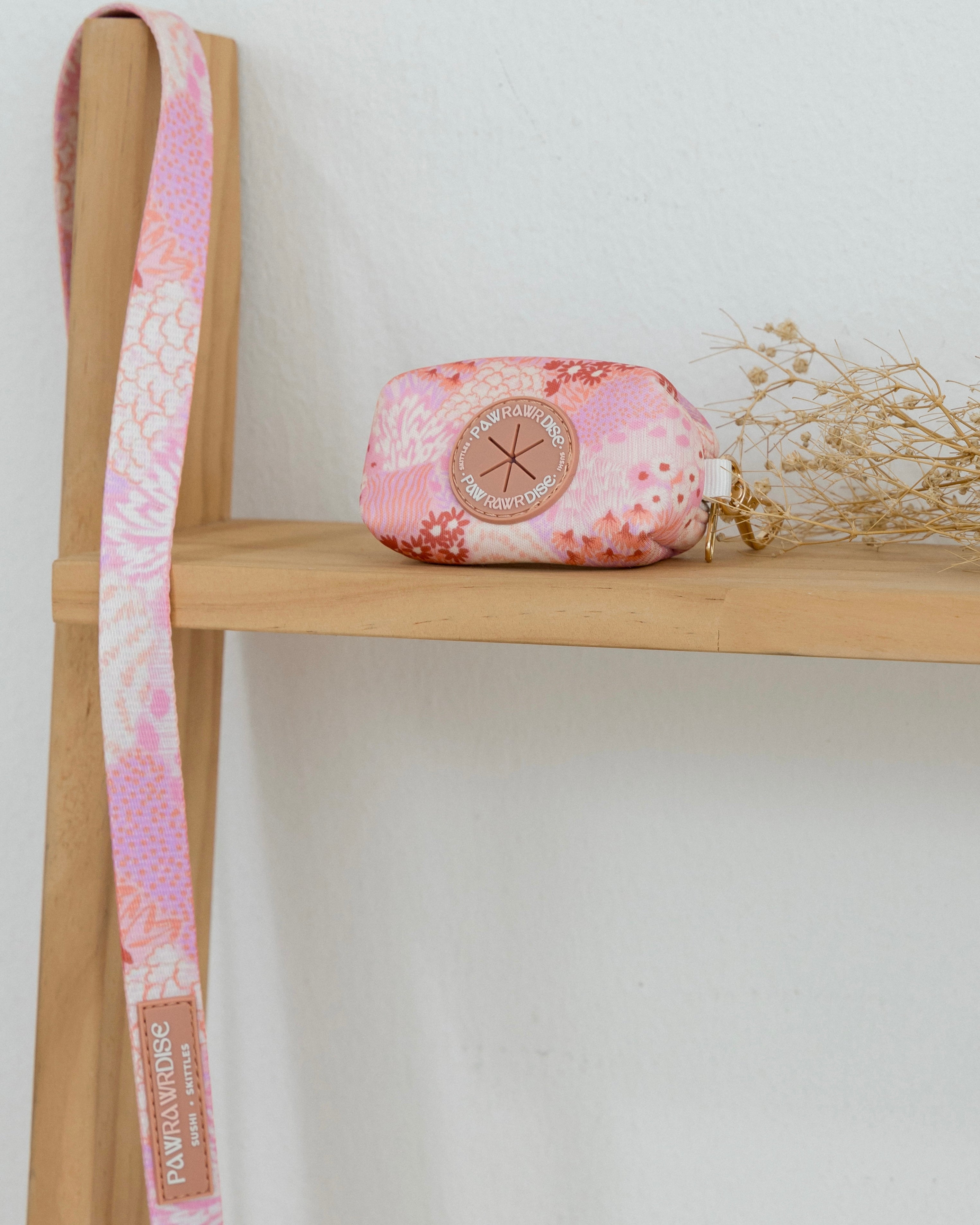 Floral-patterned pouch and strap on a wooden shelf with a white background
