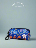 A multicolored batik print poop bag holder with a black clasp, placed against a blue background.