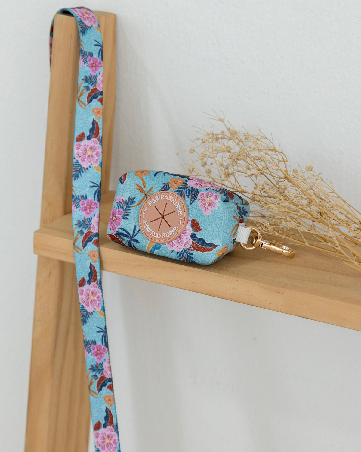 Floral-patterned pouch with strap on a wooden shelf against a white background