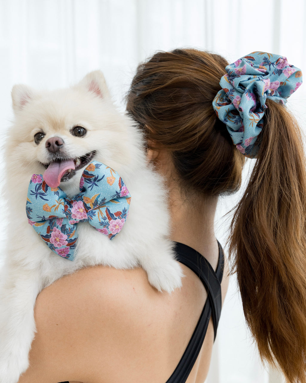 Woman holding a white pomeranian dog wearing a laguna floral bow with a matching scrunchie.