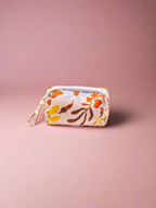Summer floral-patterned pouch with a gold zipper on a pink background